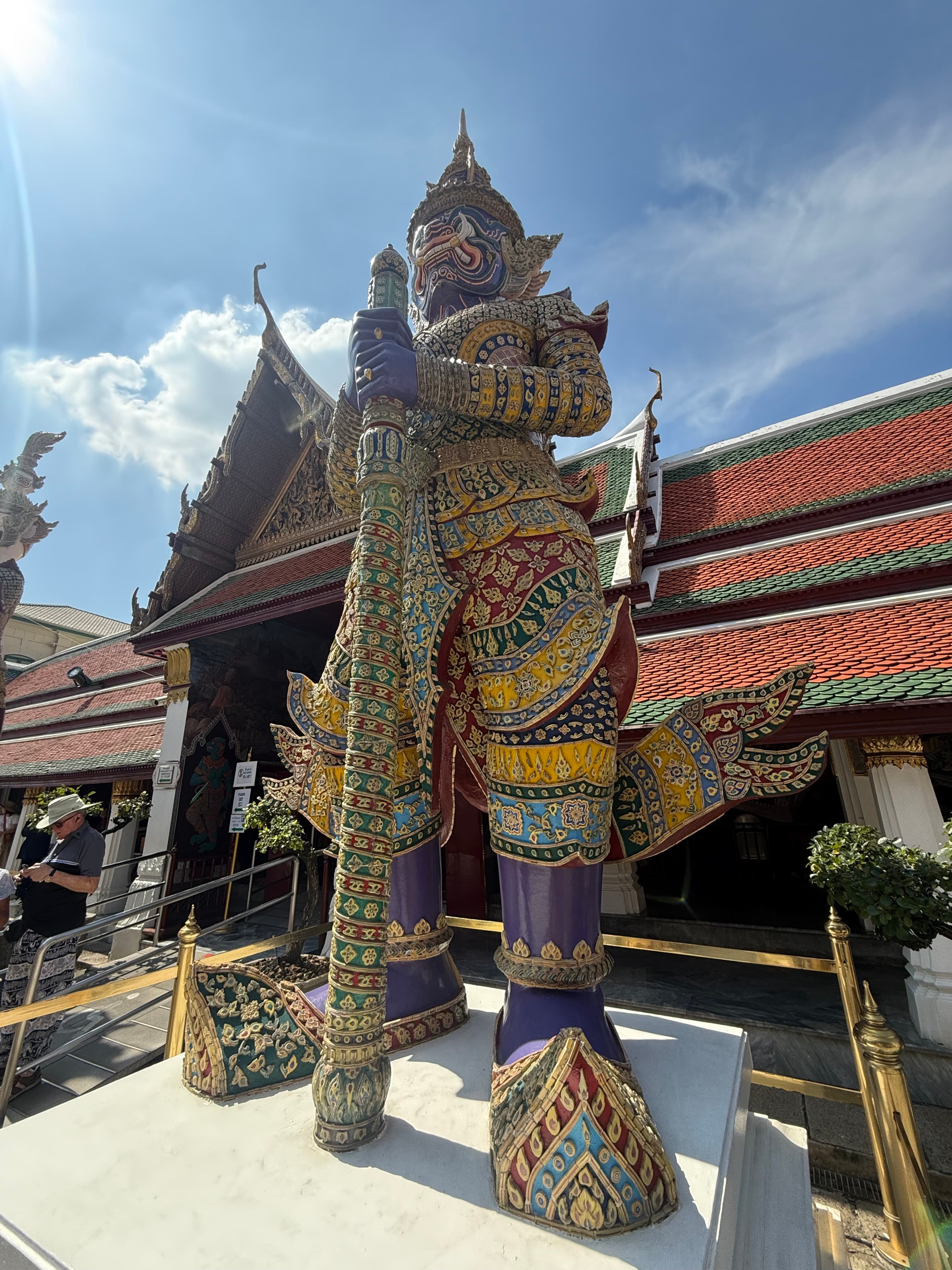 An ornate mirror-tiled yaksha guardian statue holding a club outside a temple hall at the Grand Palace in Bangkok