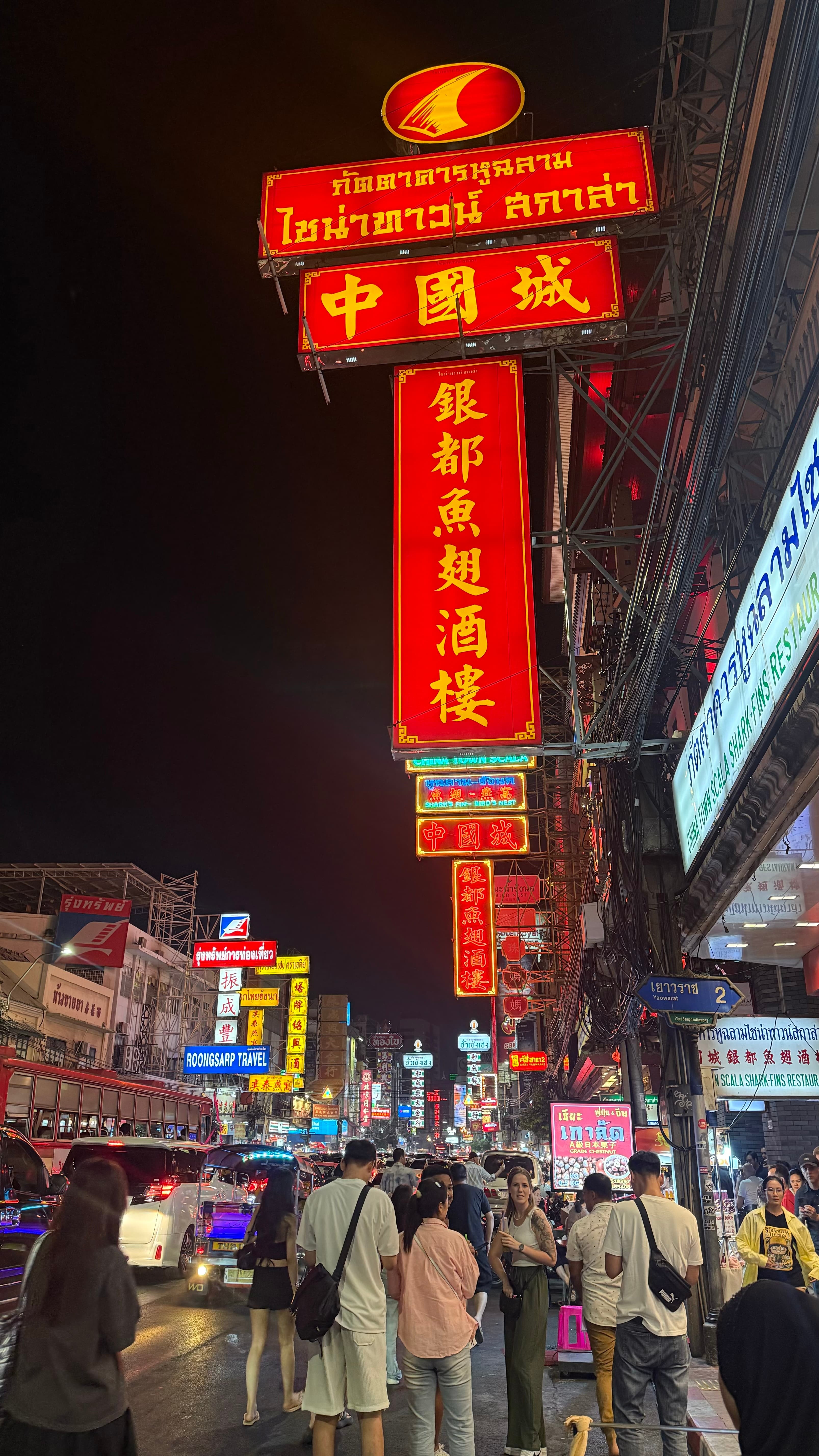 Crowds beneath towering red-and-gold neon restaurant signs on Yaowarat Road in Bangkok's Chinatown at night