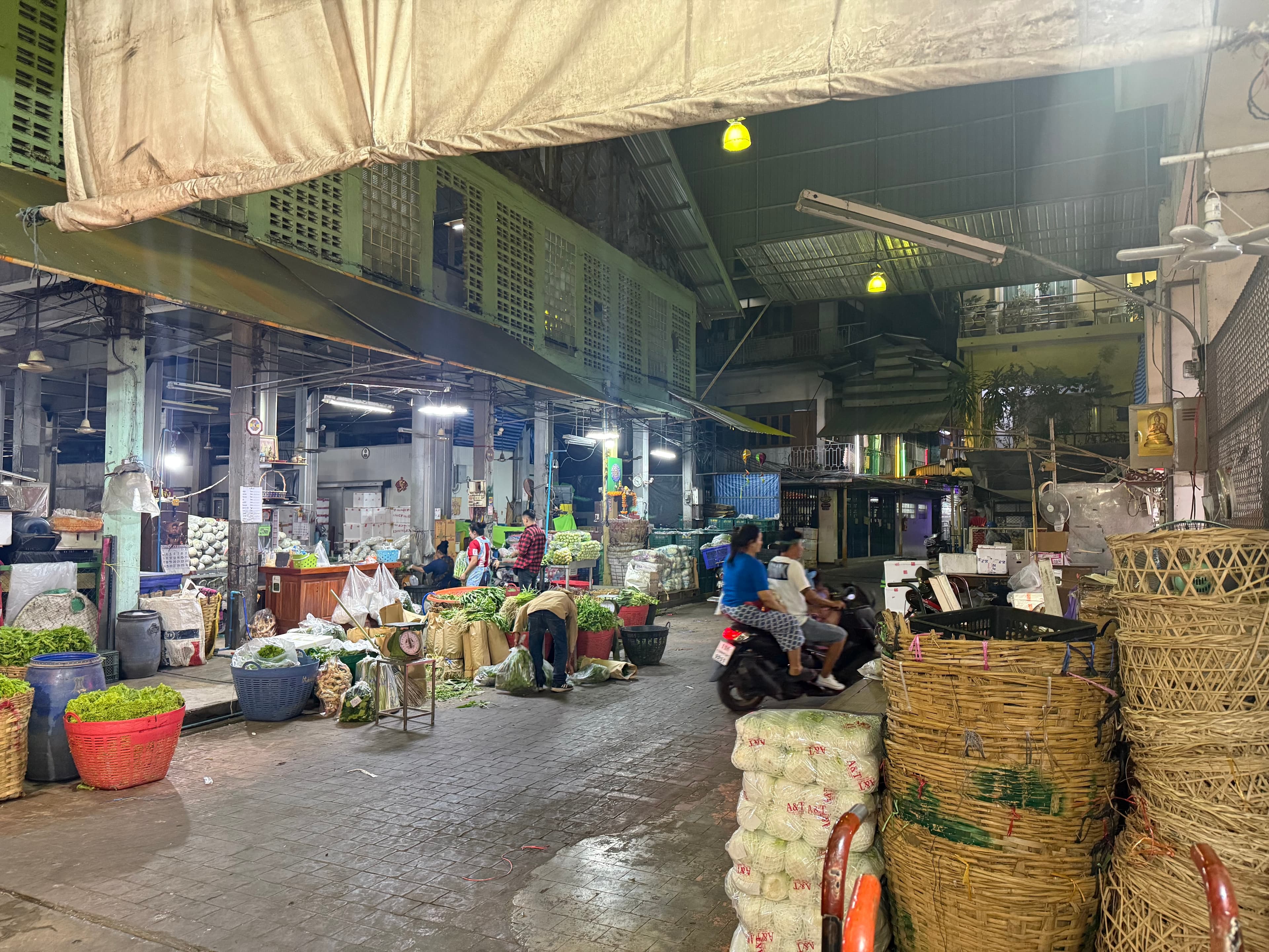 Vendors sorting fresh greens among woven baskets and sacks of cabbages at a Bangkok wholesale market