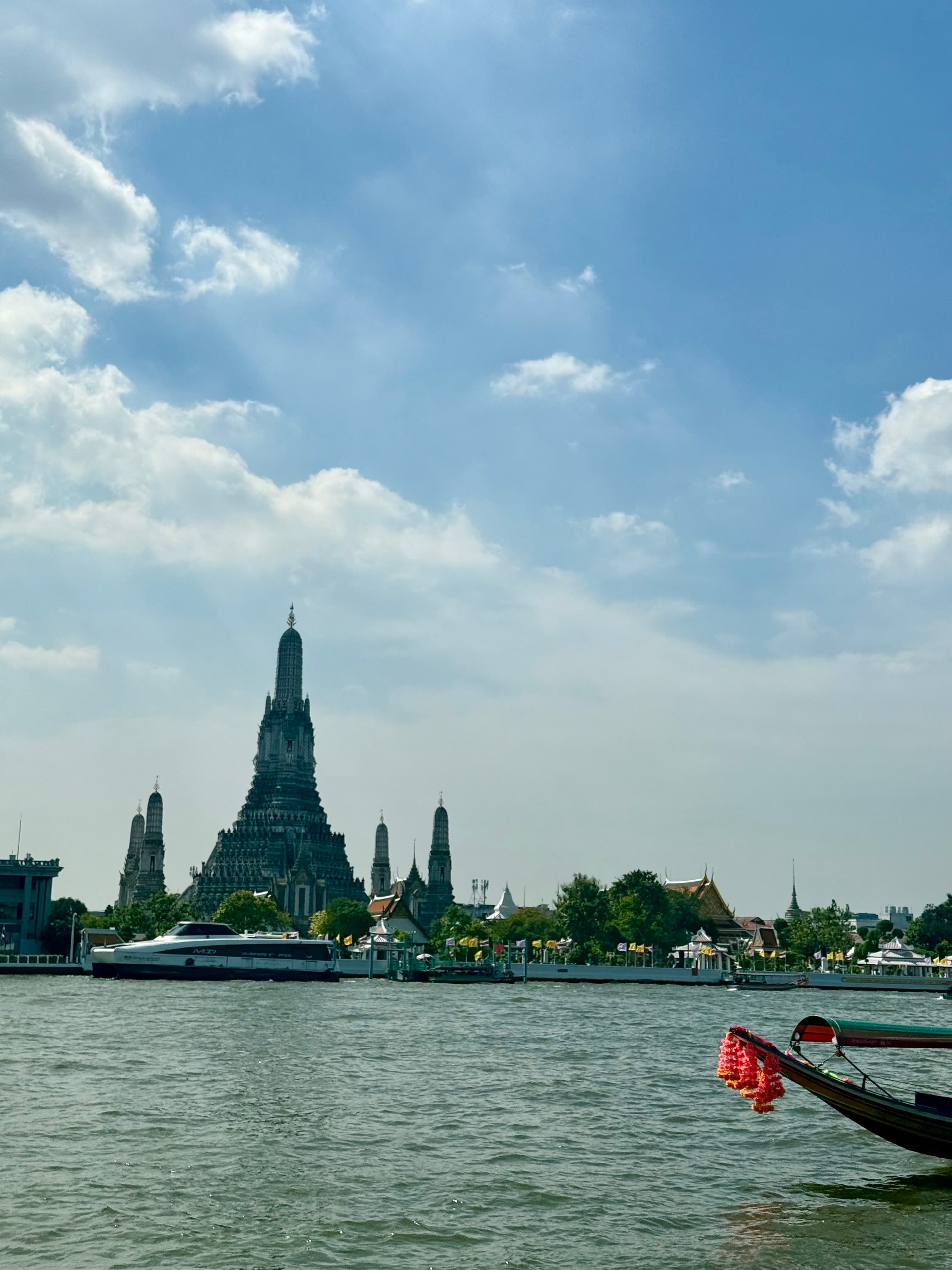 The spire of Wat Arun, the Temple of Dawn, seen across the Chao Phraya River with a flower-garlanded long-tail boat in the foreground, Bangkok
