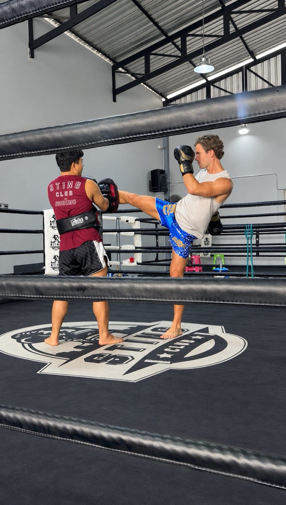 A traveler throwing a roundhouse kick at pads held by a trainer inside the ring at a Muay Thai gym in Chiang Mai