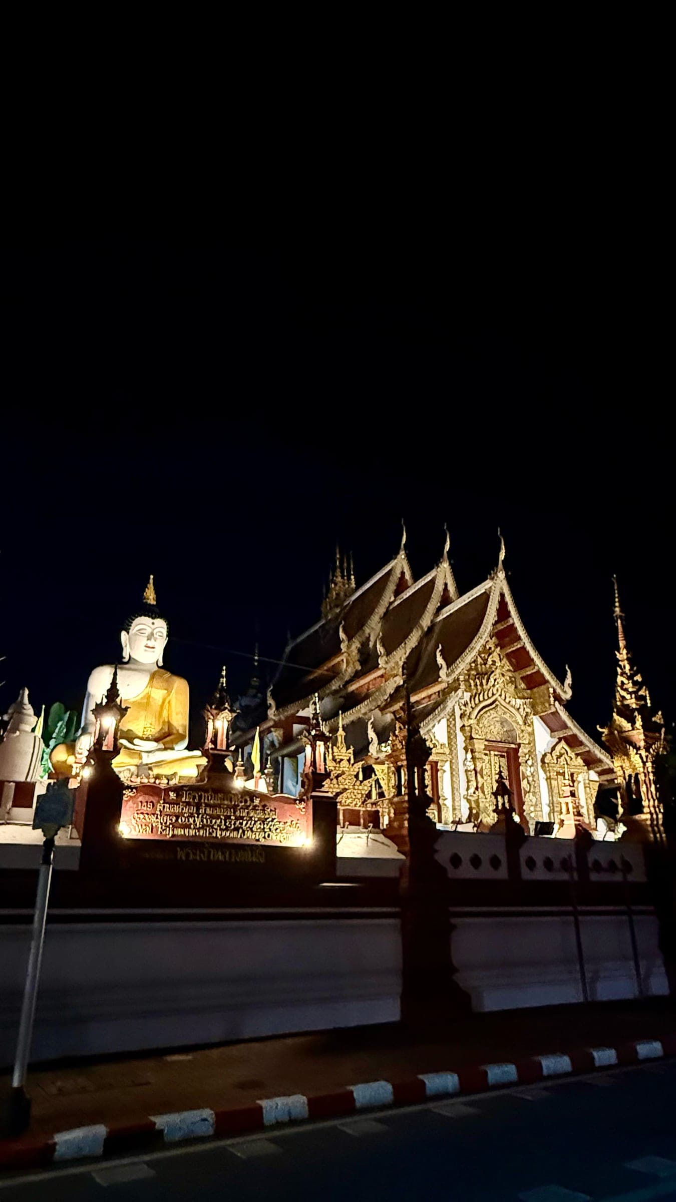Wat Rajamontean lit up at night, with tiered gold-trimmed Lanna roofs beside a giant golden seated Buddha, on the northern edge of Chiang Mai's Old City
