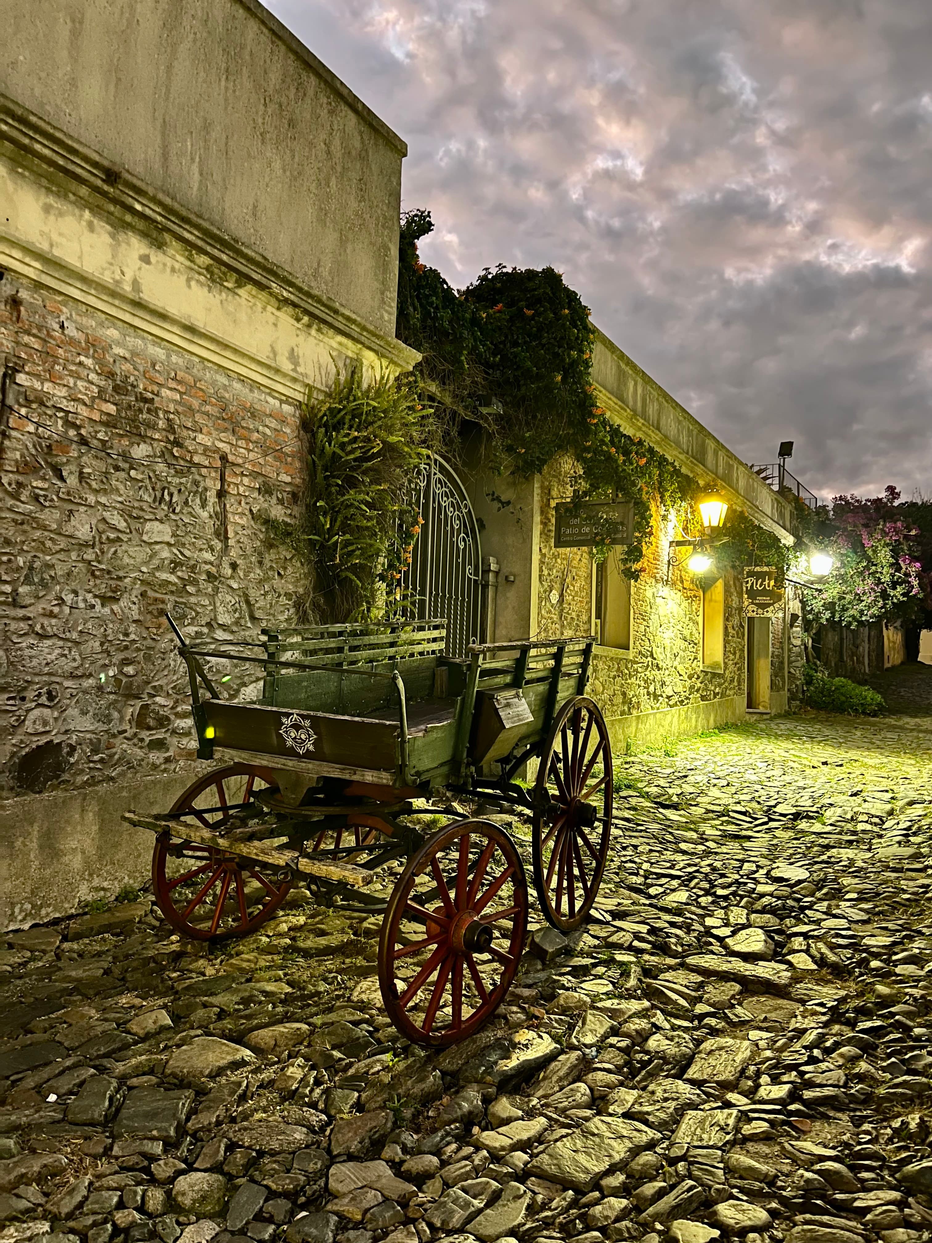 Antique horse-drawn cart on a cobblestone lane beside a stone colonial wall in Colonia's Barrio Histórico