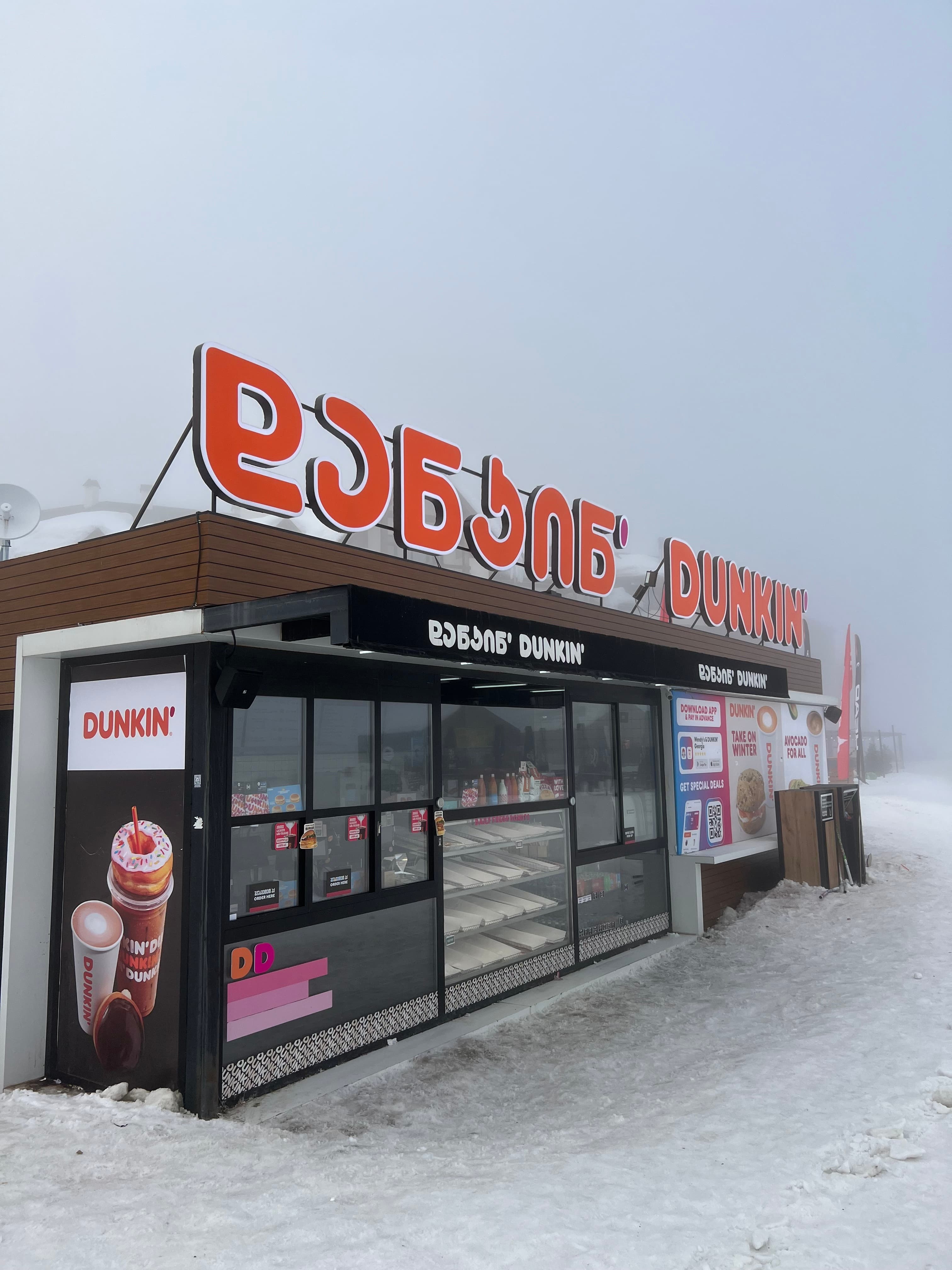 A Dunkin' kiosk with signage in Georgian and English on the fog-shrouded, snowy slopes of Gudauri