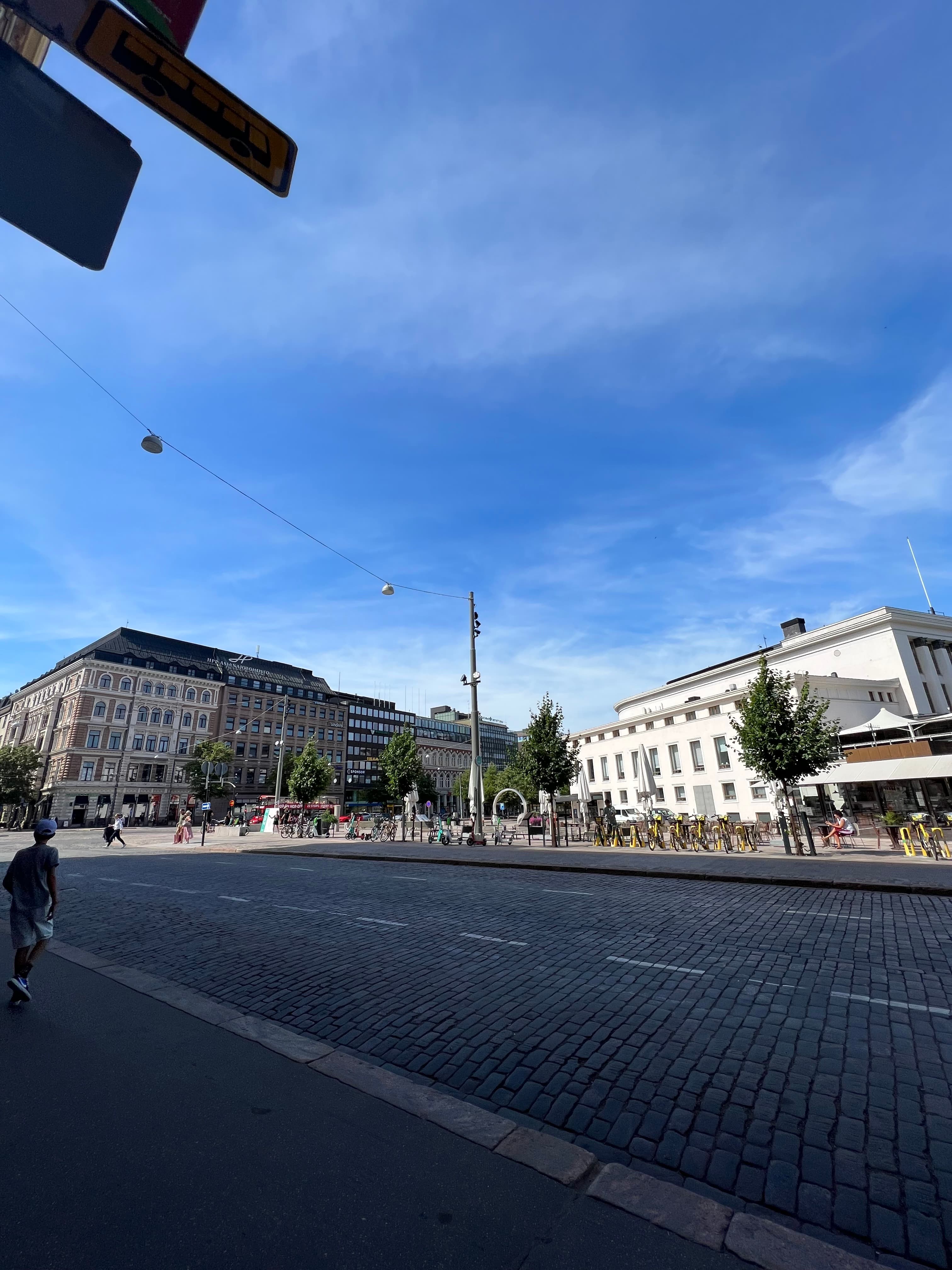 A broad cobblestone square in downtown Helsinki lined with 19th-century buildings and rows of shared city bikes and e-scooters under a blue sky