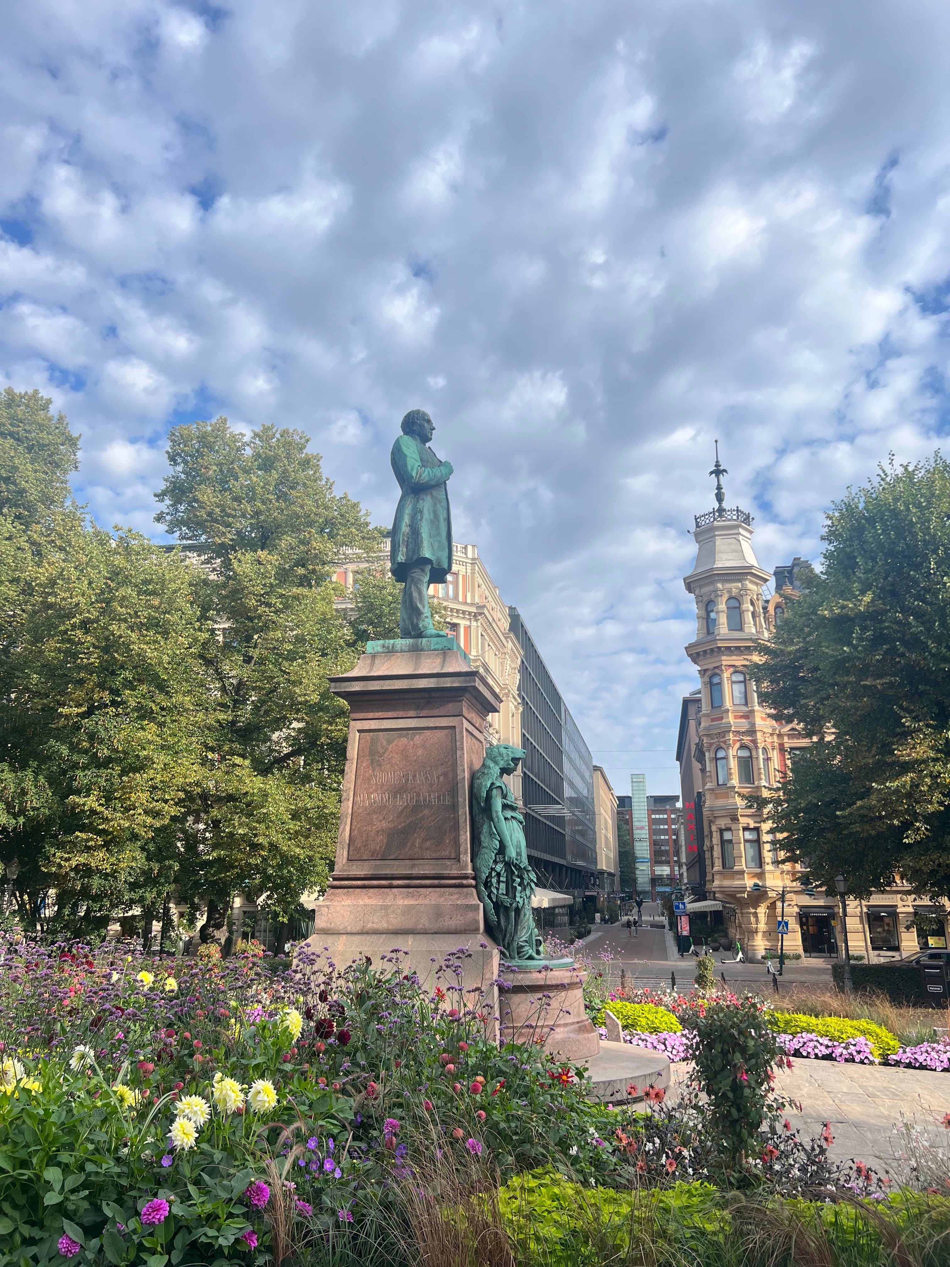 The green bronze J. L. Runeberg statue on its granite plinth amid late-summer flower beds in the Esplanadi park, central Helsinki
