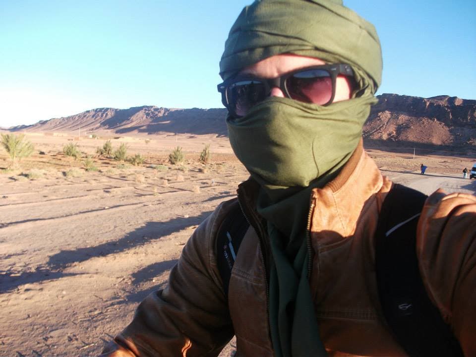 Traveler wrapped in a green desert headscarf and sunglasses on the camel trek out of Zagora, Morocco