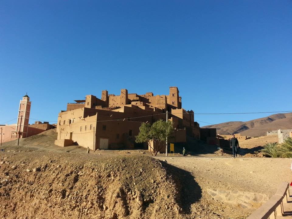 A red mud-brick kasbah on a rise beside a village minaret in Morocco's Draa Valley