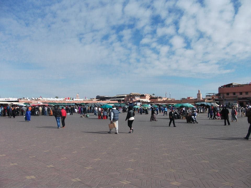 Crowds and green-roofed food stalls filling the Jemaa el-Fna square in Marrakesh, with the Koutoubia minaret on the skyline