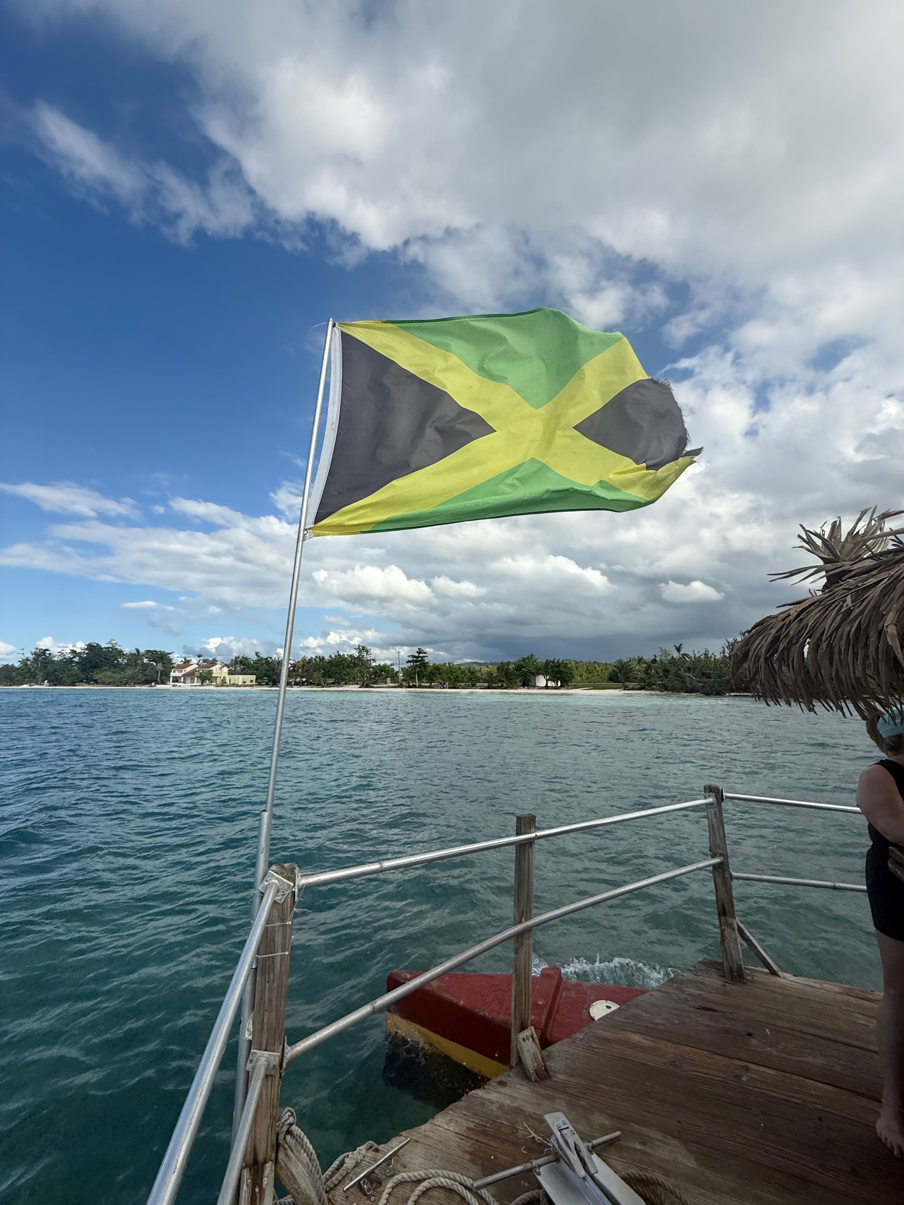 A Jamaican flag flying off the back of a boat over turquoise water along the Negril coastline
