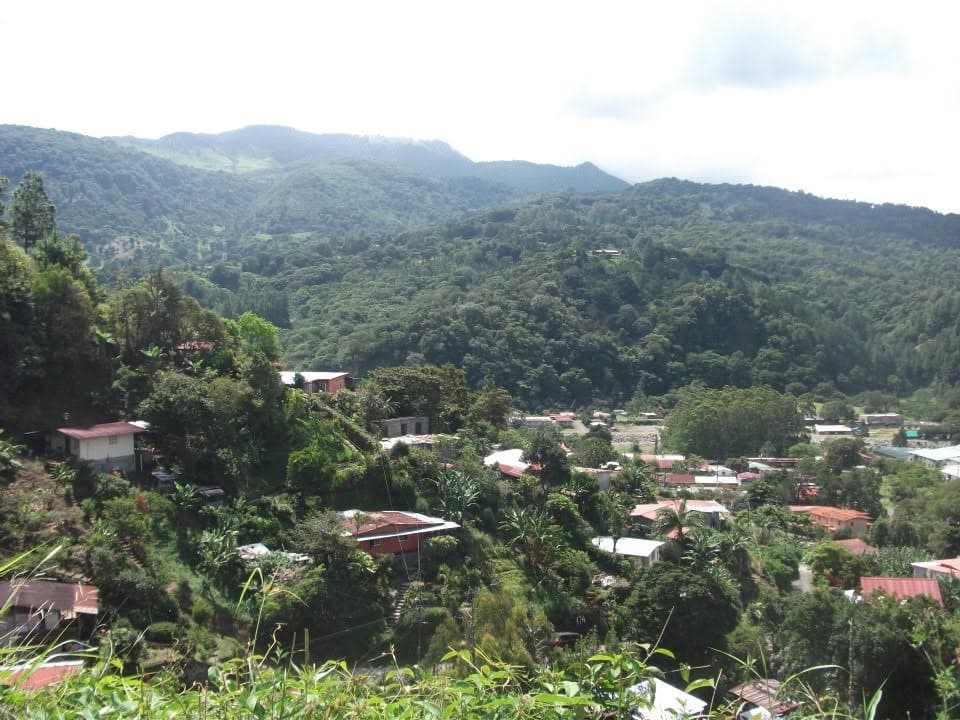 Red- and tin-roofed houses scattered down a forested valley below green mountains in the Boquete highlands