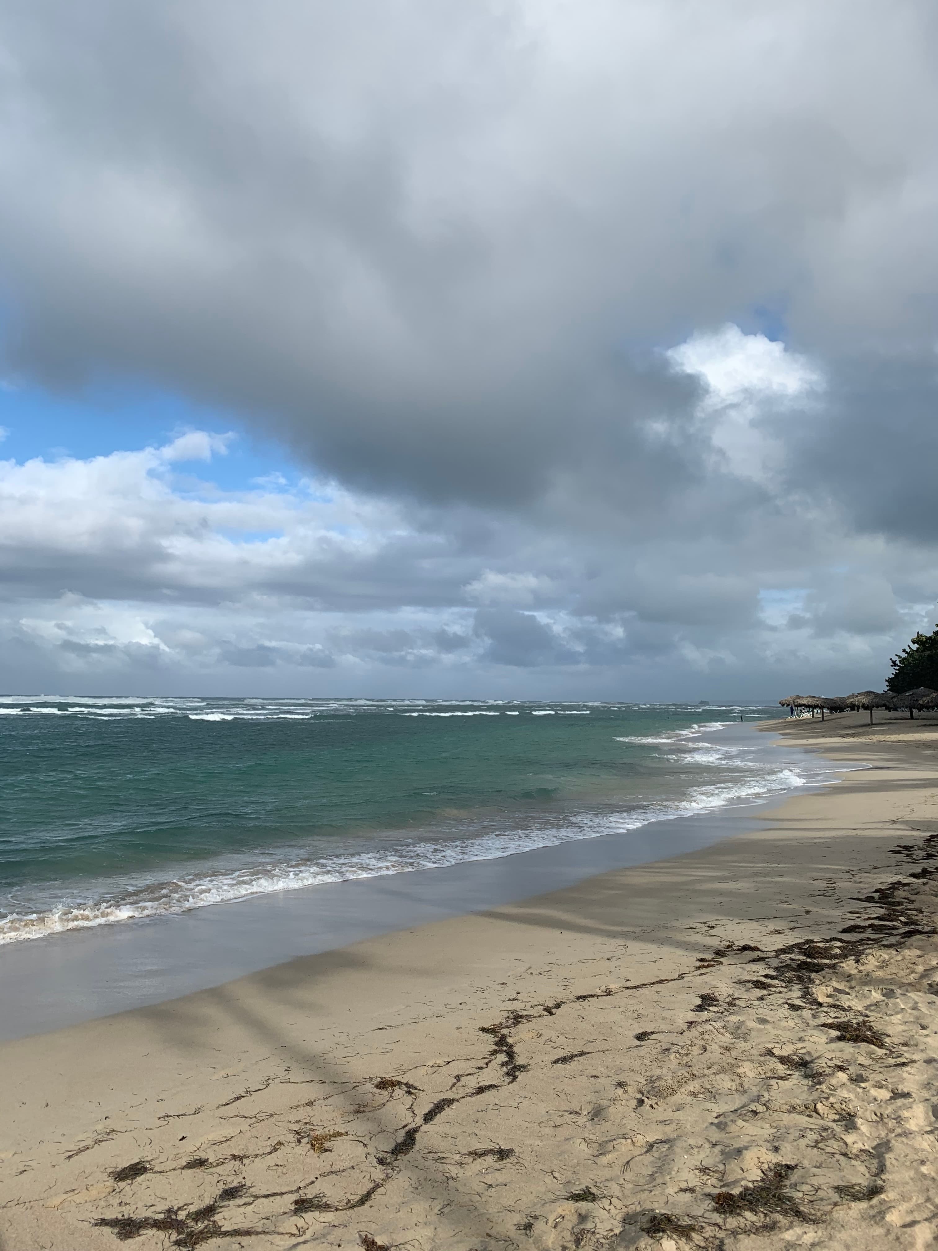Breaking turquoise surf along a wide sandy beach lined with thatched umbrellas under a dramatic cloudy sky on the north coast near Puerto Plata