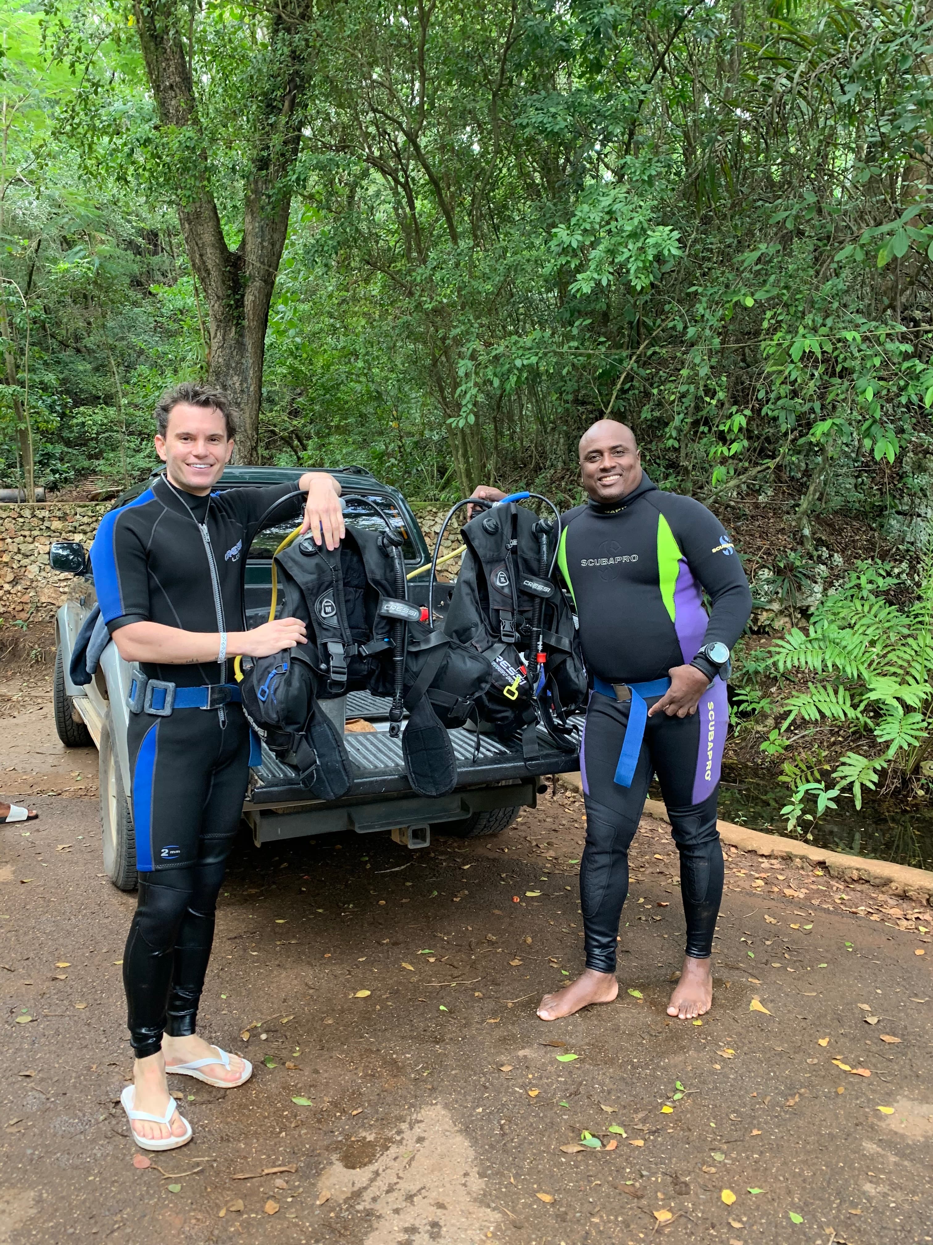 Two divers in wetsuits standing with scuba gear loaded on a pickup truck bed before a dive near Puerto Plata