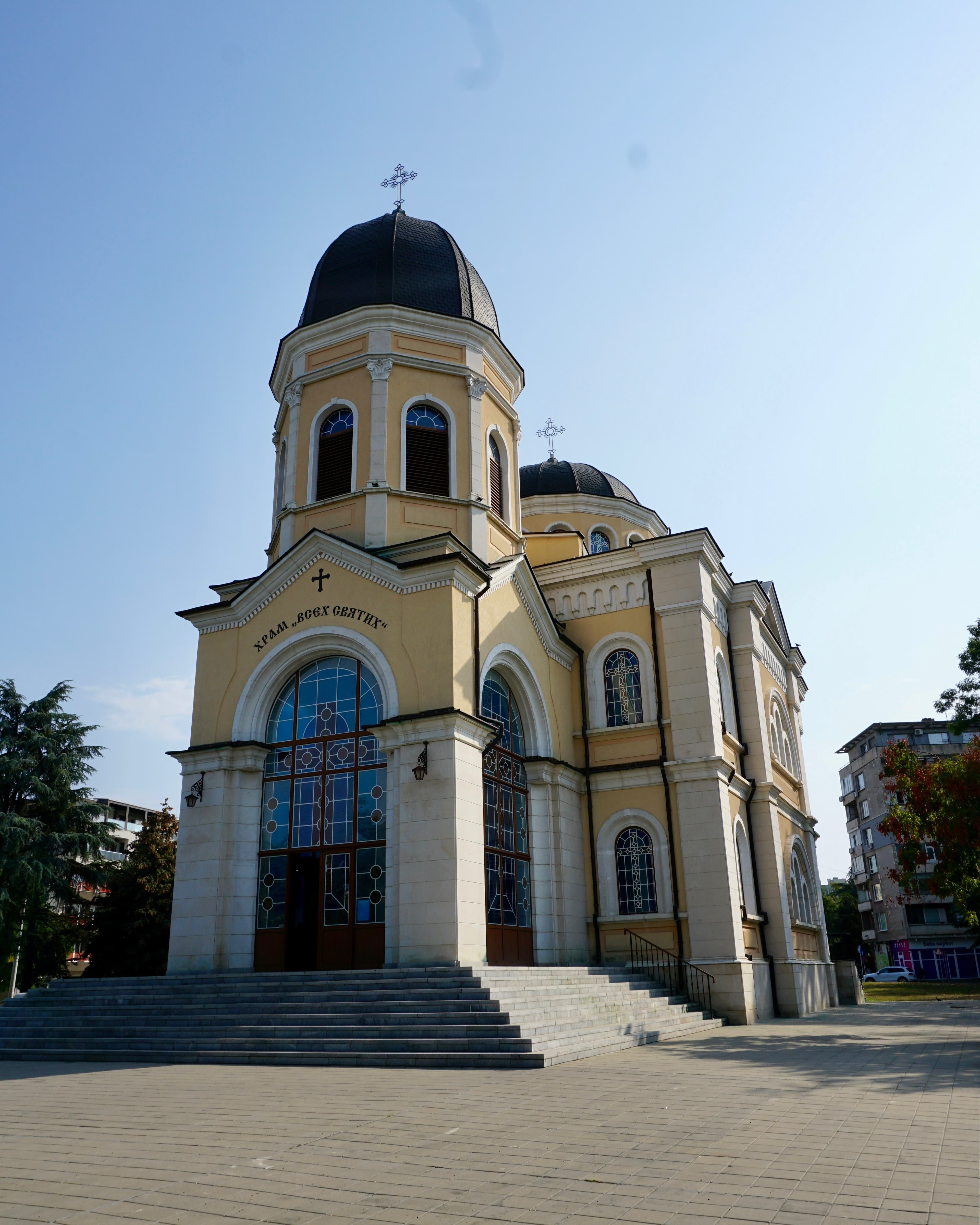 The All Saints Orthodox church in Ruse, a yellow-and-white building with dark domes and tall stained-glass windows