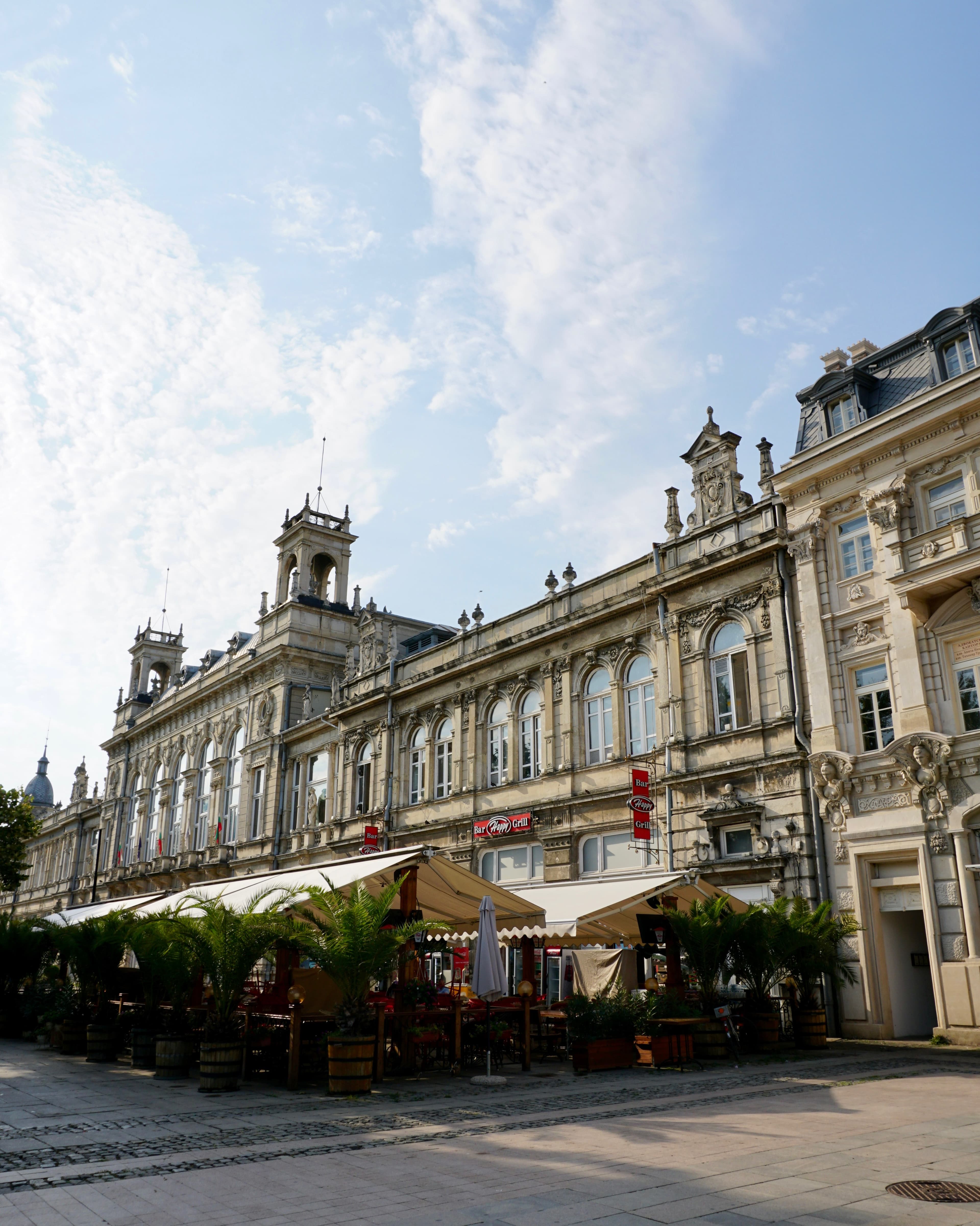 A row of ornate neo-baroque facades along Ruse's pedestrian street, with a sidewalk cafe under awnings