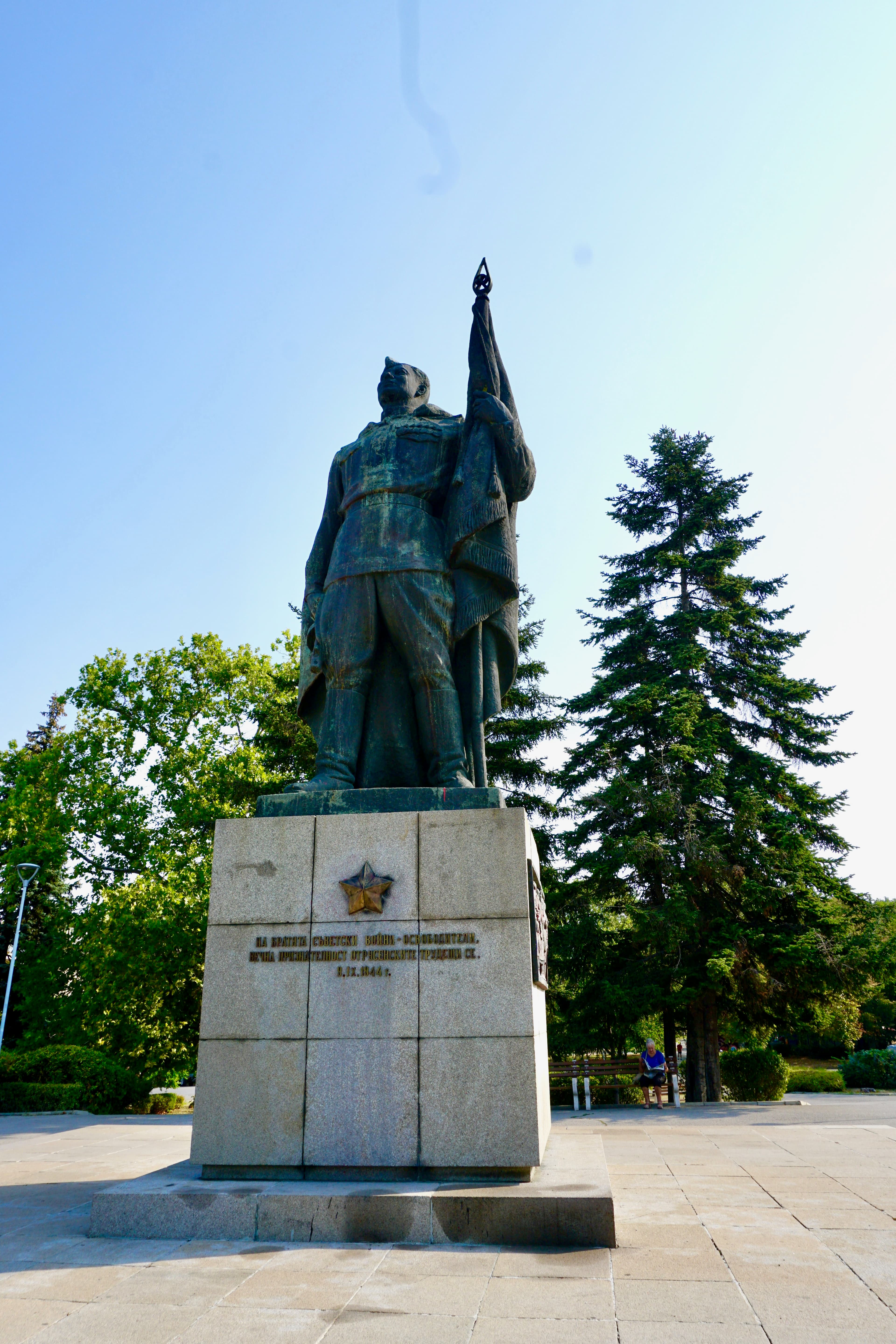 A bronze Soviet soldier monument raising a flag on a granite plinth marked with a Soviet star, commemorating 1944, in a Ruse park