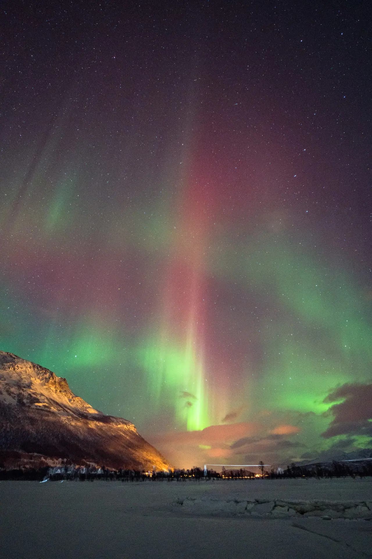 Red and green aurora pillars rising over a frozen fjord near Tromsø