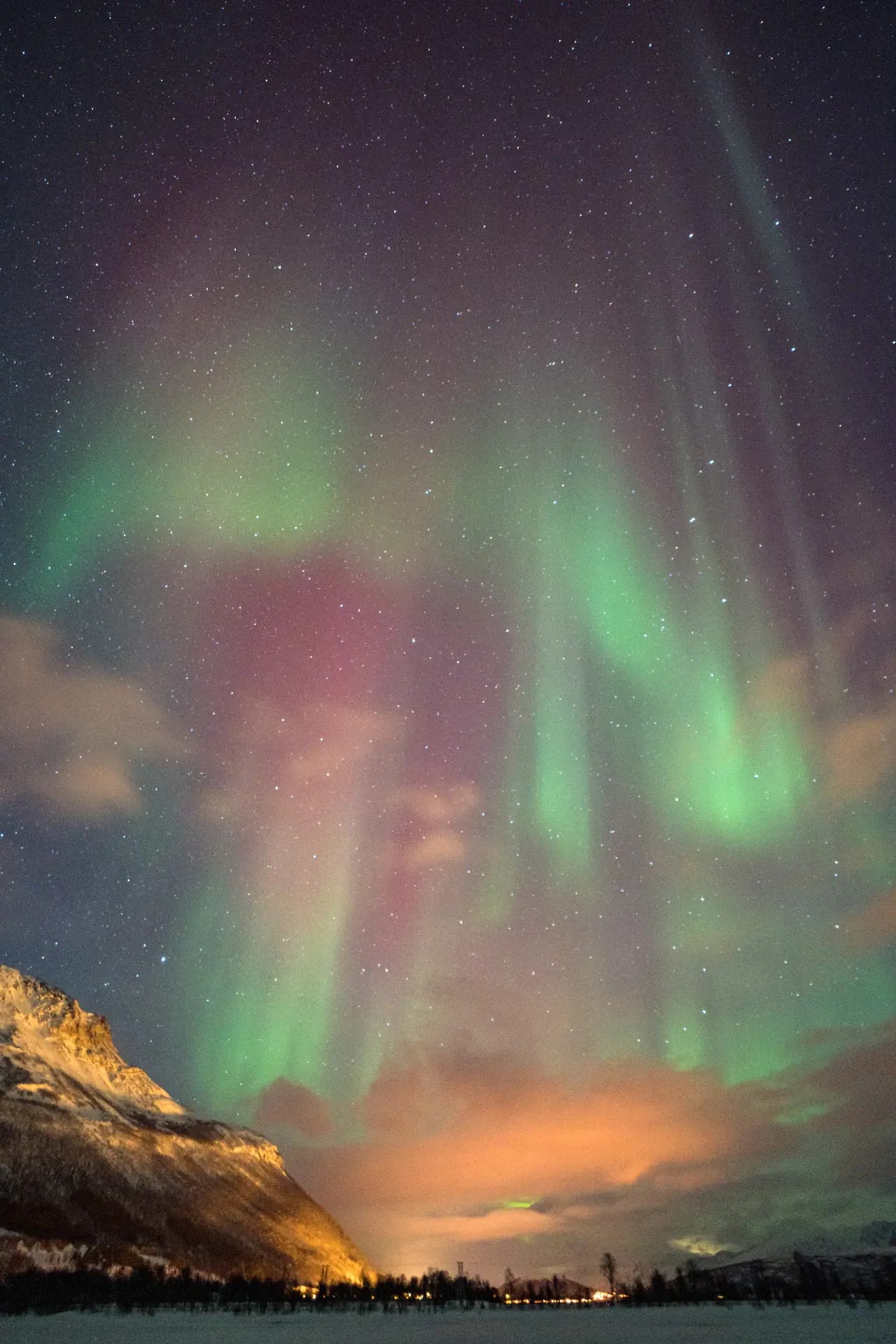 Northern lights mixed with star-filled sky above mountains in Tromsø