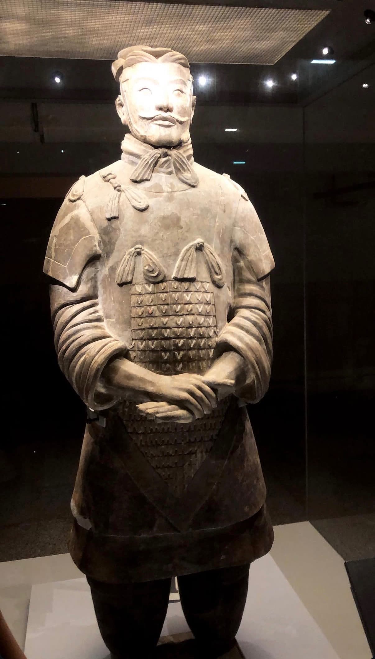 A single well-preserved terracotta warrior with laced armor and a knotted scarf displayed under glass at the Terracotta Army museum in Xi'an