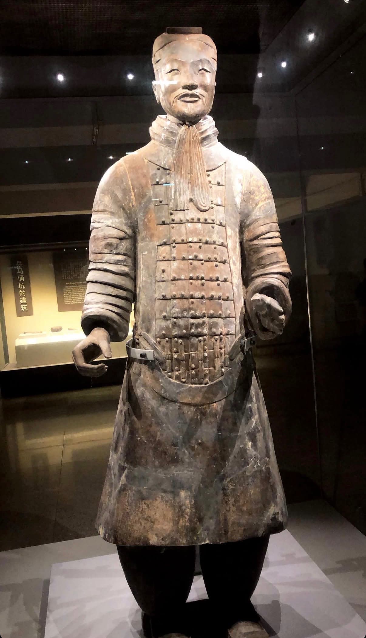 An armored terracotta soldier figure with riveted plate and topknot displayed in a case at the Terracotta Army museum near Xi'an