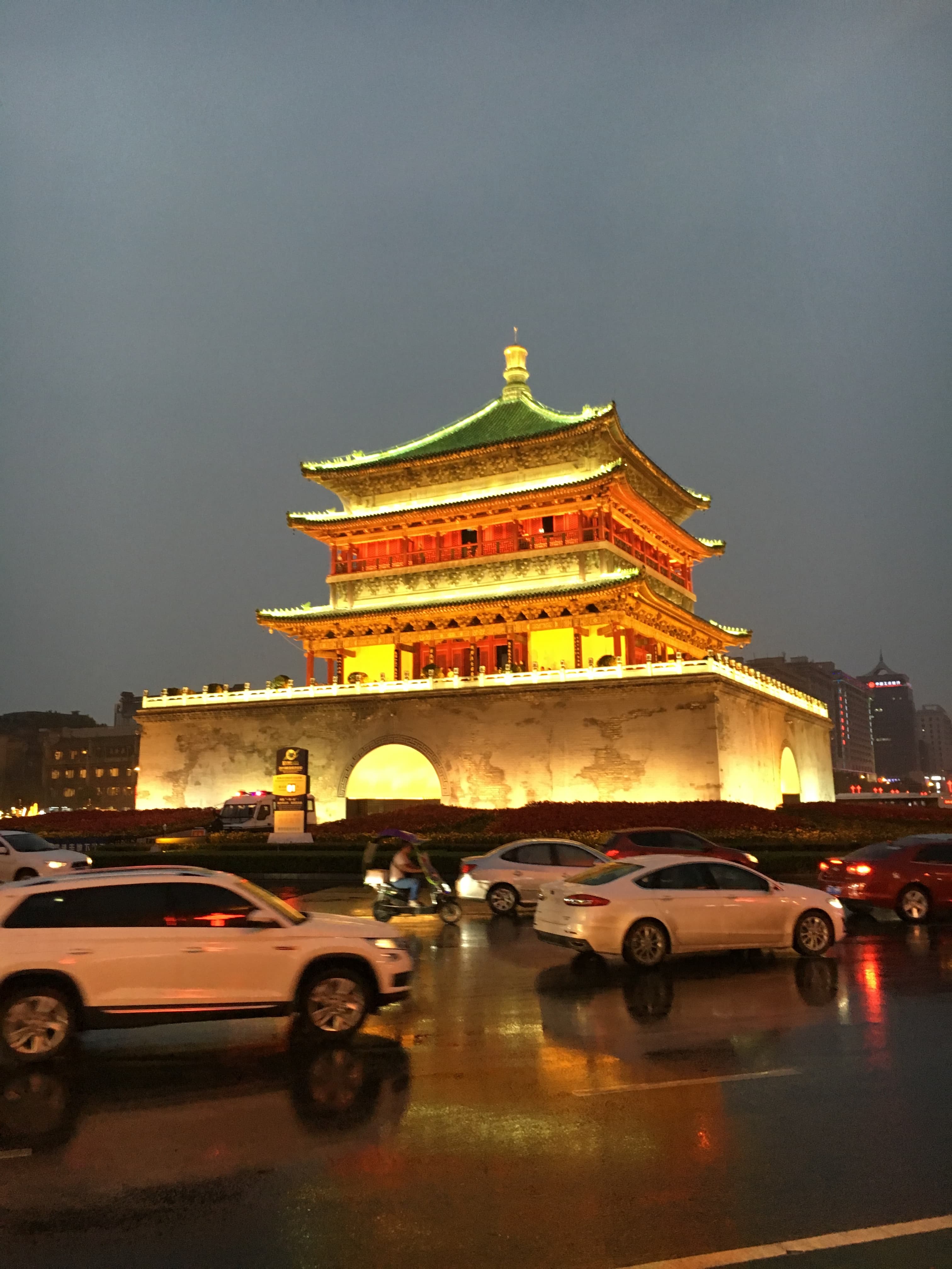 The Bell Tower of Xi'an lit up at dusk above traffic on a rain-slicked square